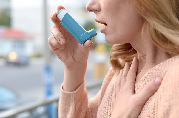 Woman using asthma inhaler outdoors, closeup. 